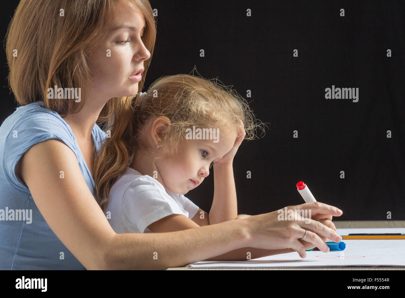 Side view of mother assisting girl in drawing against black background Stock Photo