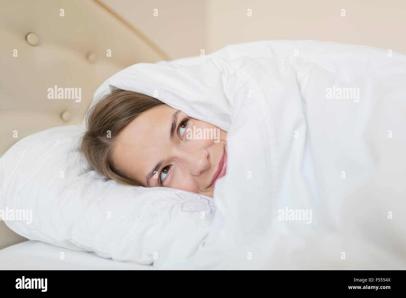 Thoughtful woman covered with duvet looking away while relaxing in bed at home Stock Photo