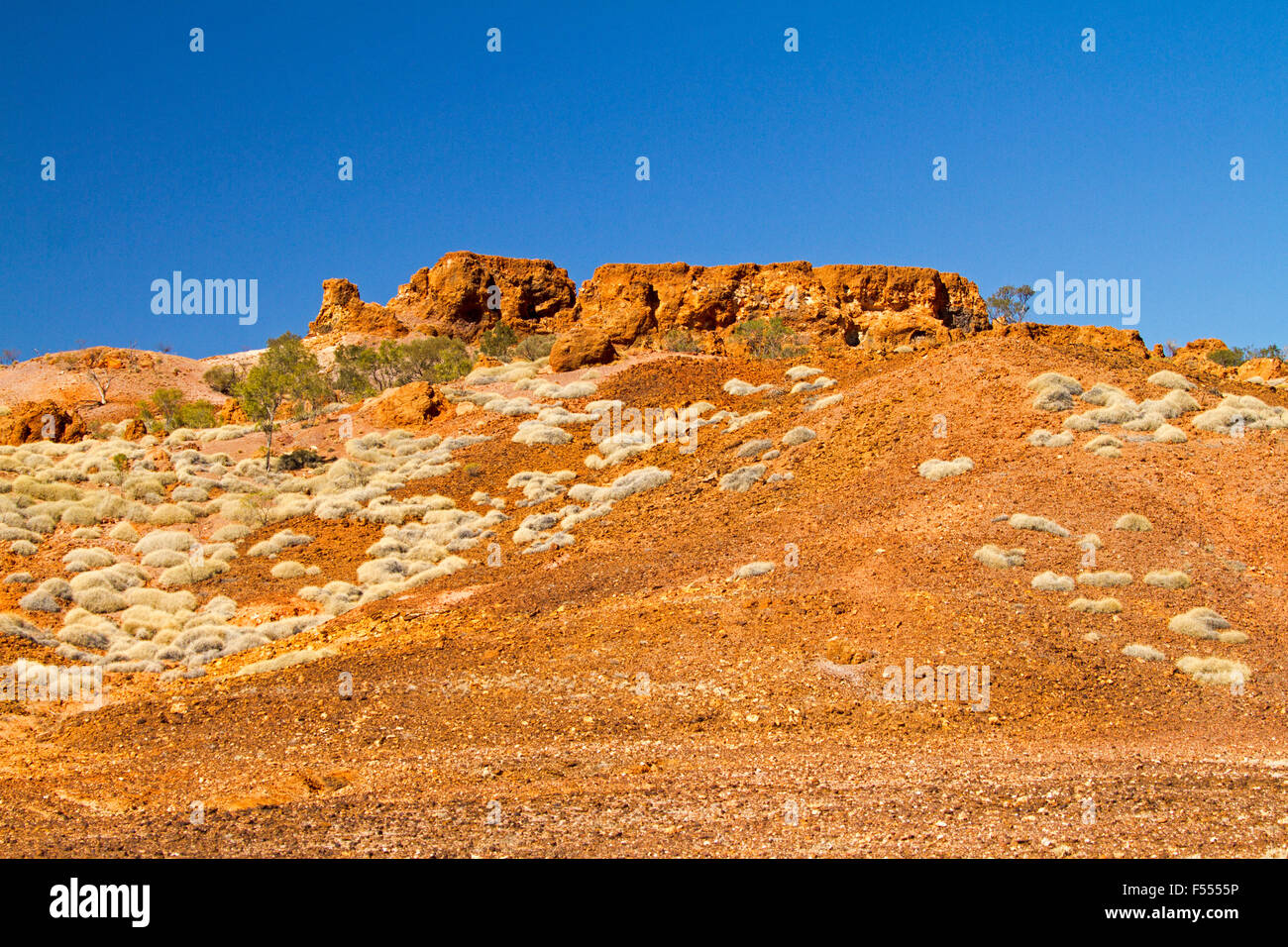 Australian outback landscape with rugged red rocky hill and barren slopes cloaked with spinifex grass under blue sky Stock Photo