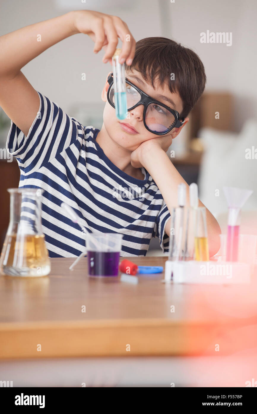 Boy wearing protective eyewear looking at test tube in house Stock Photo