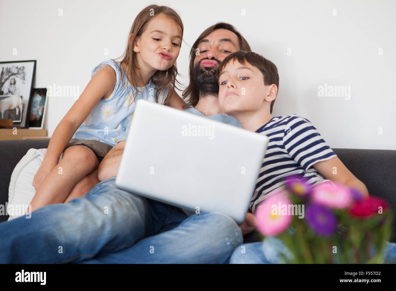 Father with children puckering in front of laptop while sitting on sofa Stock Photo