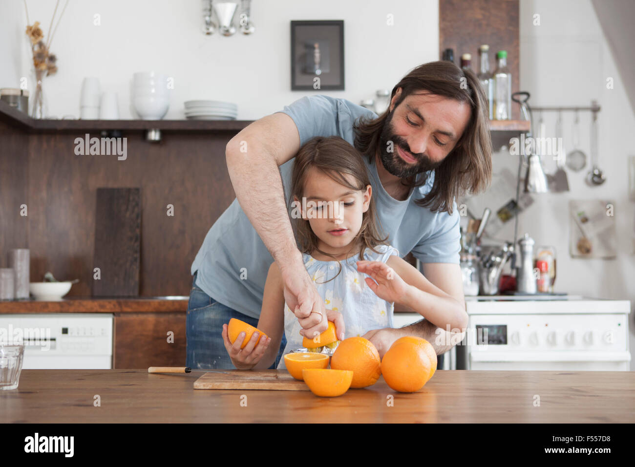 Father assisting daughter squeeze oranges in kitchen Stock Photo