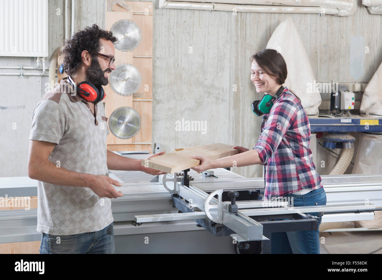 Carpenters laughing while using sliding table saw in workshop Stock Photo
