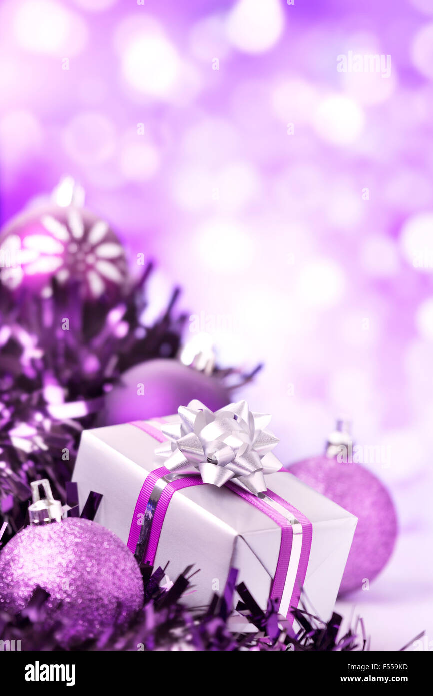 Purple and silver Christmas baubles and a gift in front of defocused purple and white lights. Stock Photo