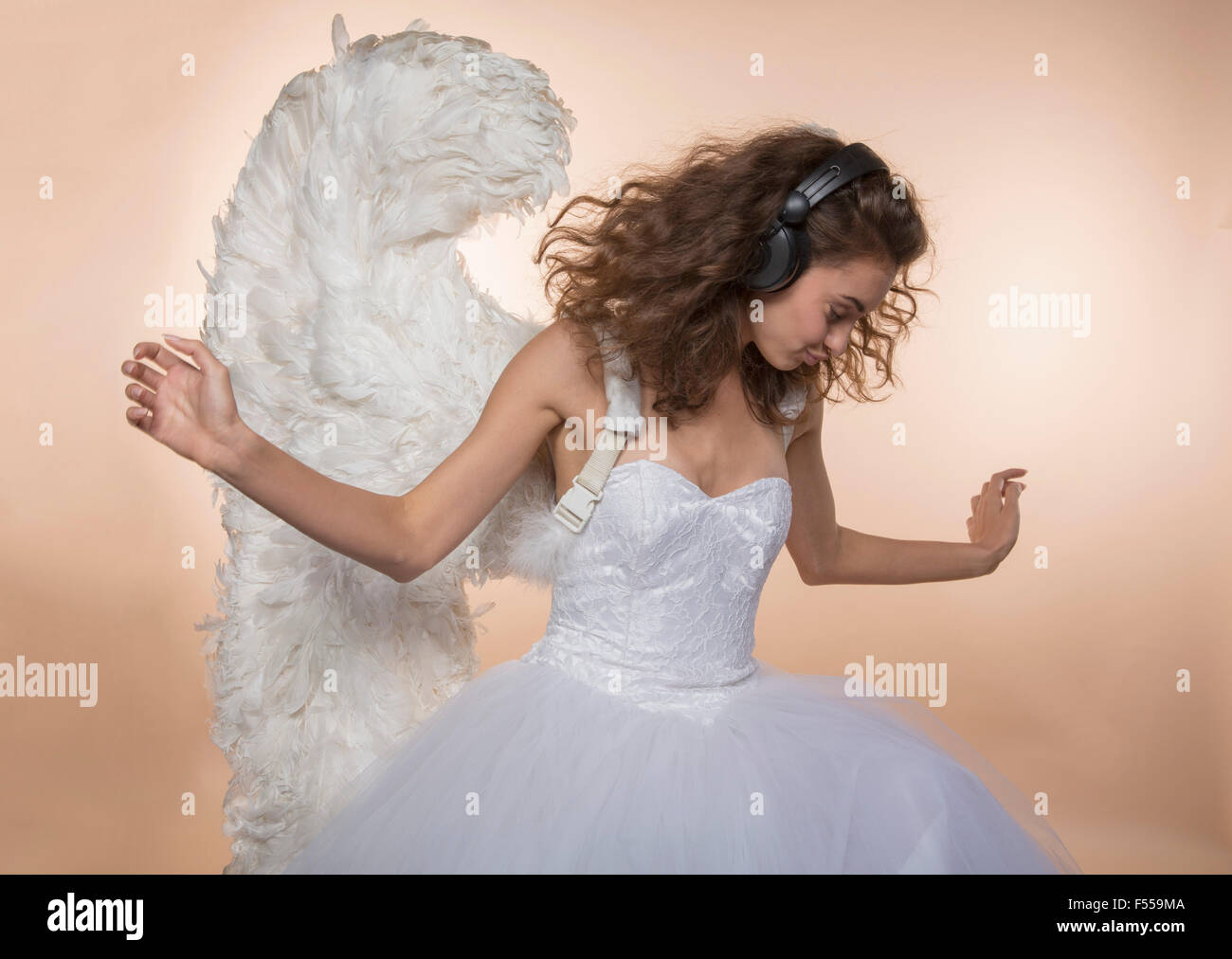 Bride in angel wings dancing while listening music against colored background Stock Photo