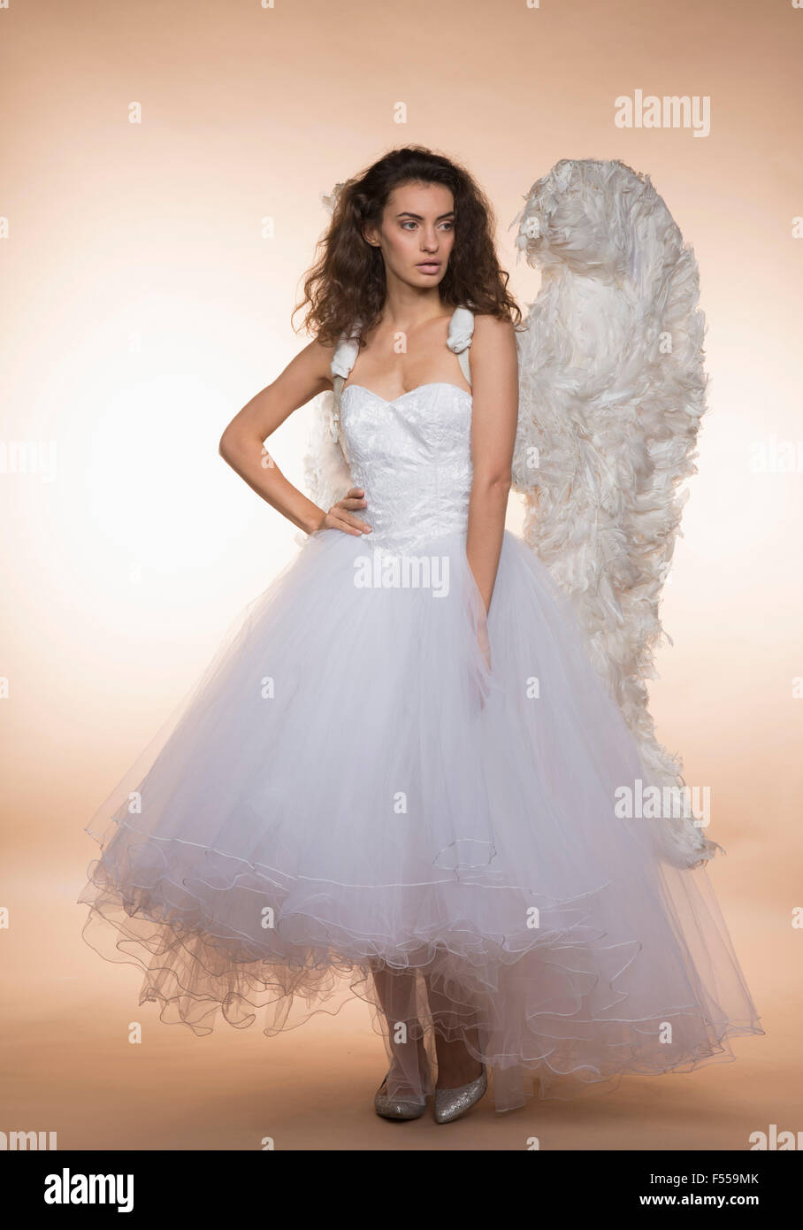 Confident bride in angel wings standing against colored background Stock Photo