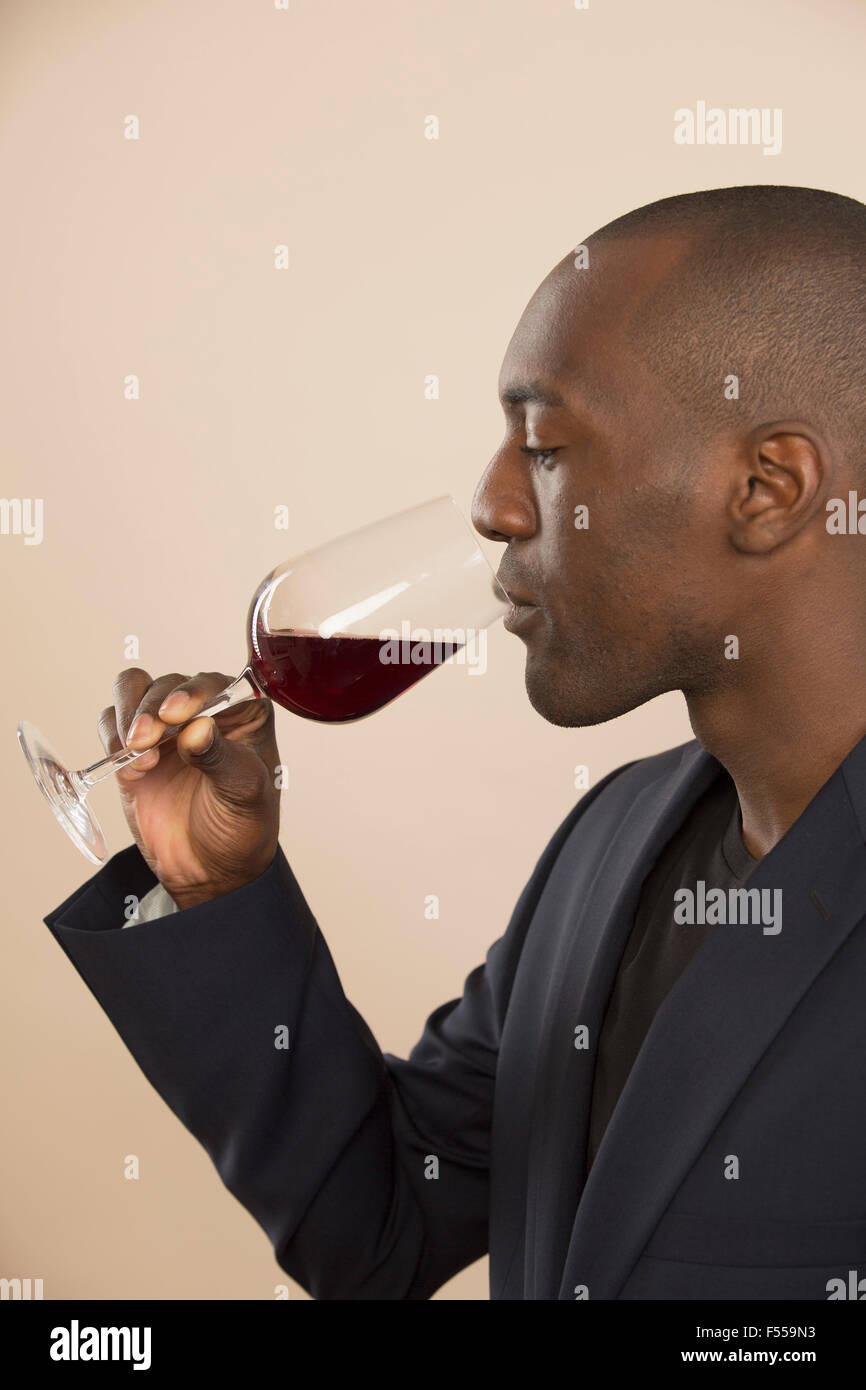 Well-dressed man tasting red wine against colored background Stock Photo