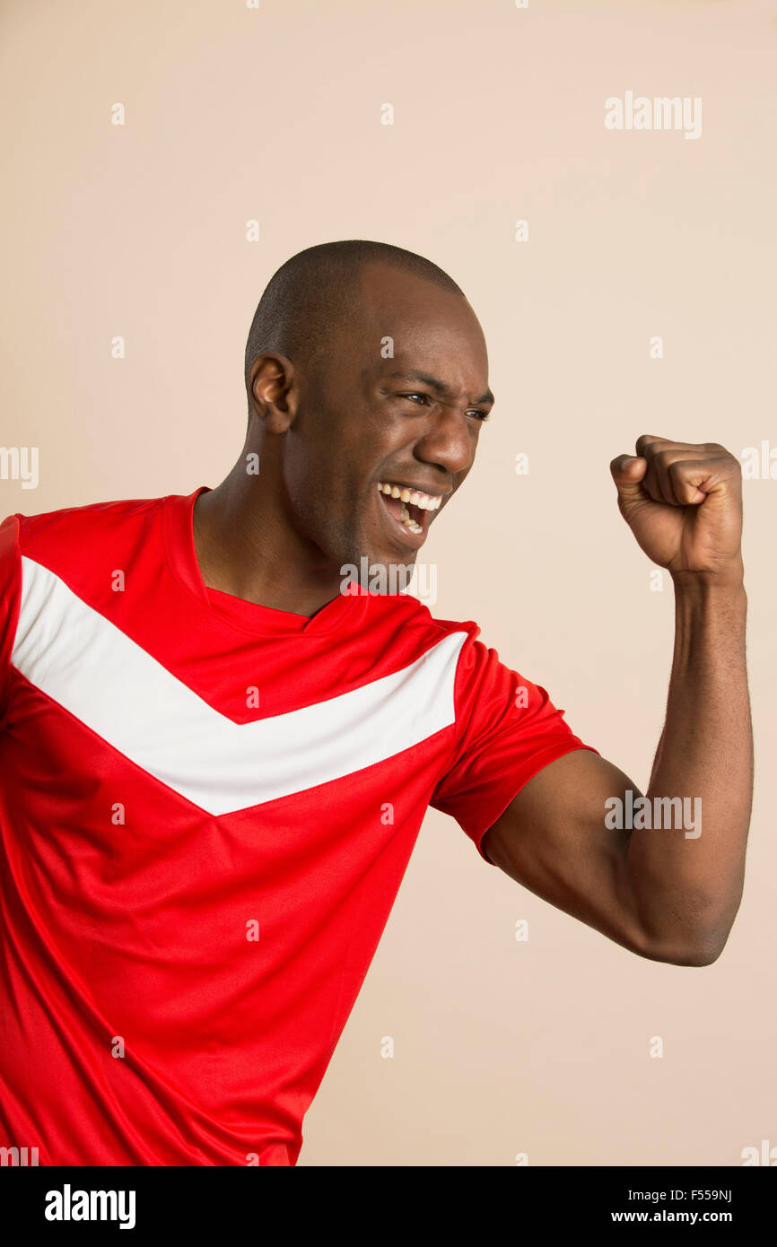 Enthusiastic soccer player with clenched fist against colored background Stock Photo