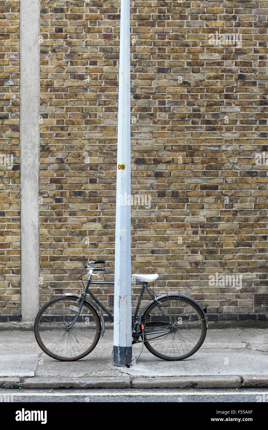 Bicycle locked up to pole on sidewalk Stock Photo