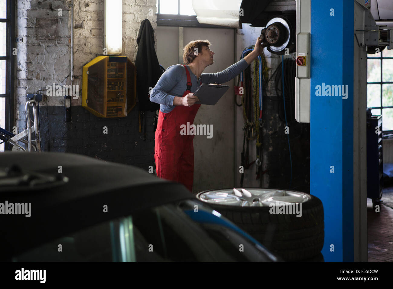 Mechanic examining car while holding clipboard at garage Stock Photo