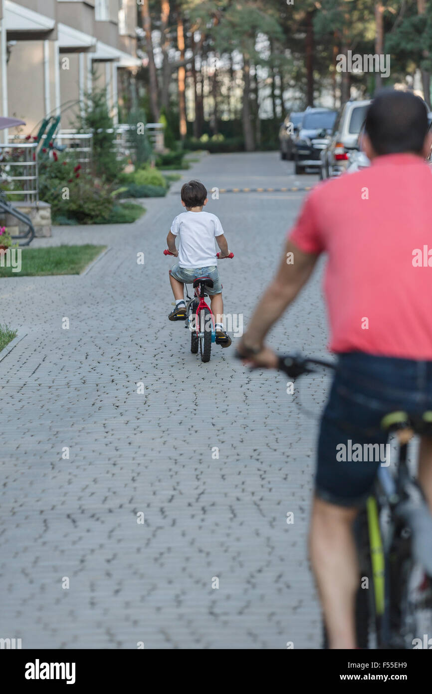 Rear view of father and son riding bicycle on street Stock Photo