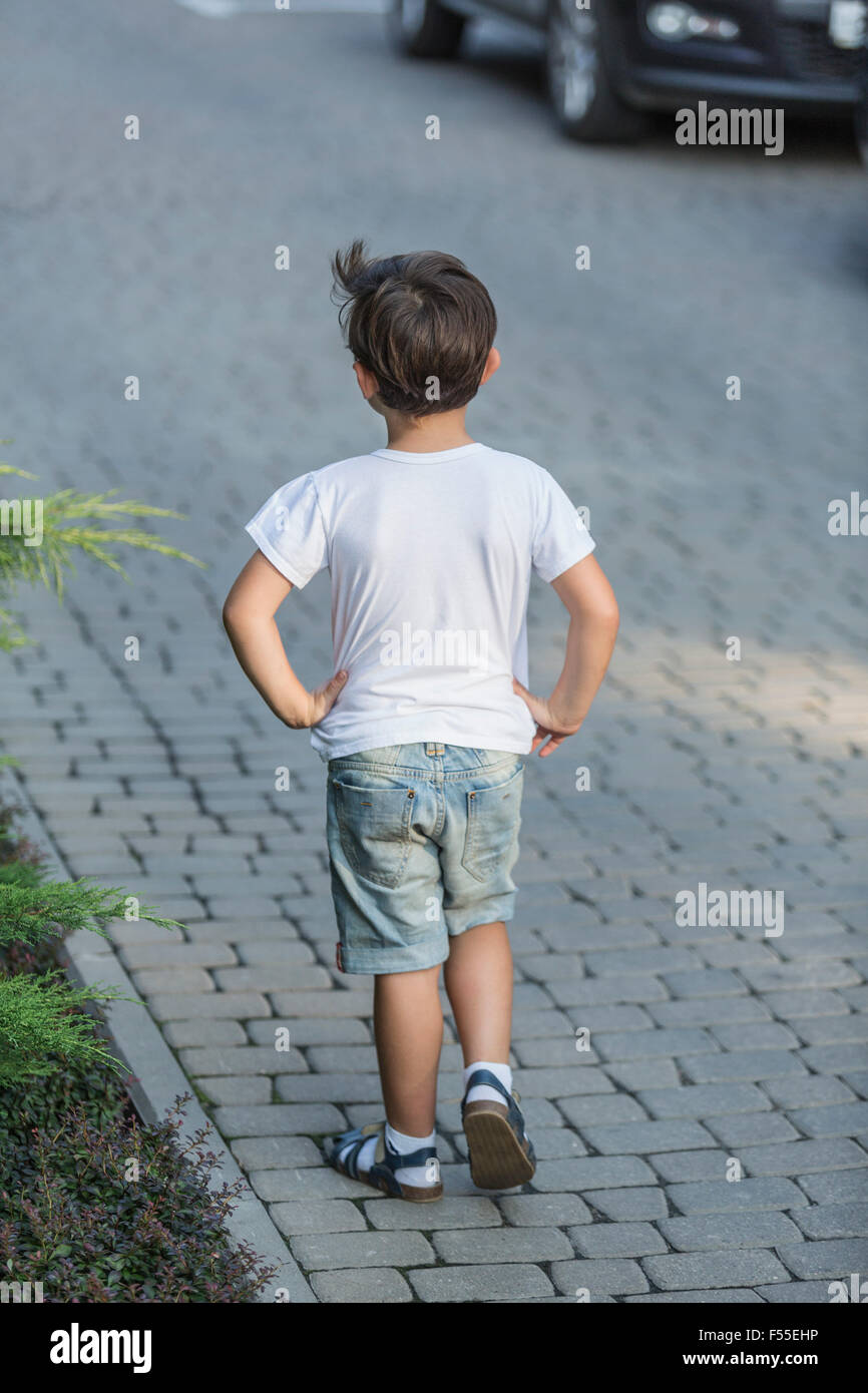 Rear view of boy with hands on hip standing on street Stock Photo