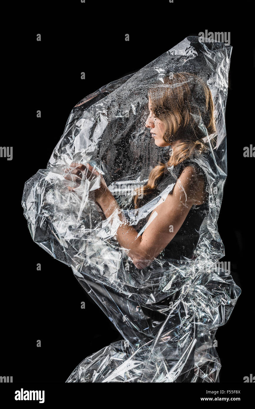 Woman wrapped in plastic standing against black background Stock Photo