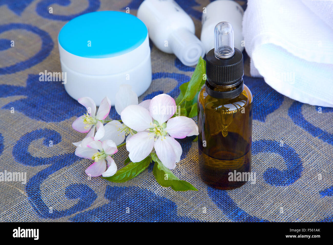 A dropper bottle of apple blossoms extract and apple blossoms on a sack cloth. Cream box,body lotion,white towels in the backgro Stock Photo