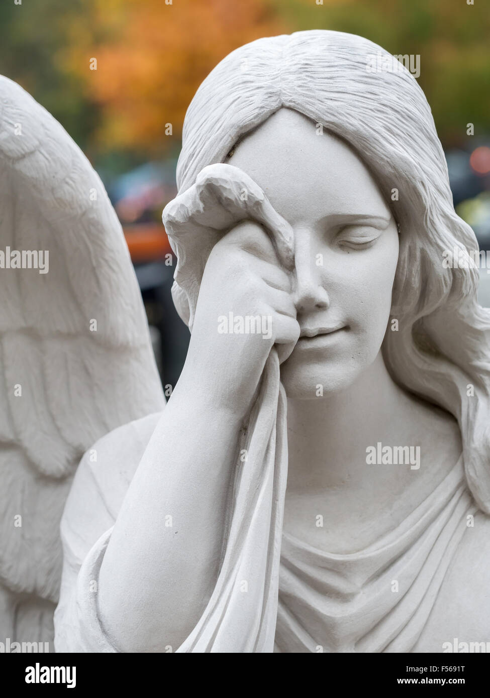 Closeup of white stone mourning angel statue on tombstone Stock Photo