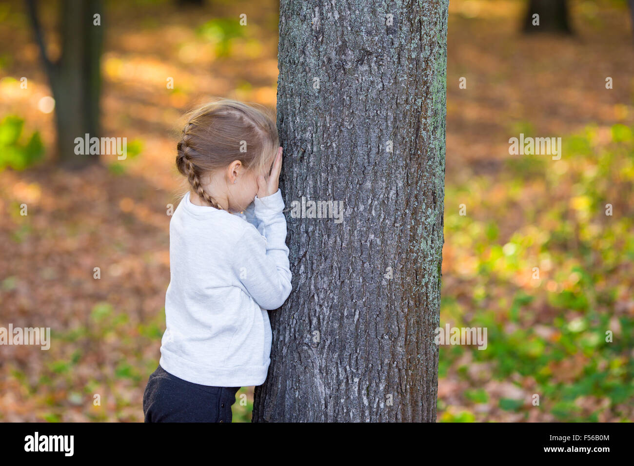 Гулять в прятки. ПРЯТКИ В парке. Маленькая девочка возле дерева. Девочка играет в ПРЯТКИ. Маленькая девочка возле парка.