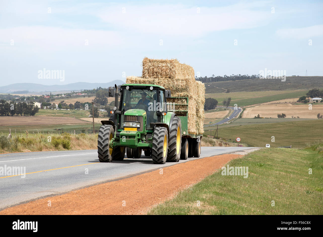 Farm tractor and trailer pulling a load of straw on a public road in