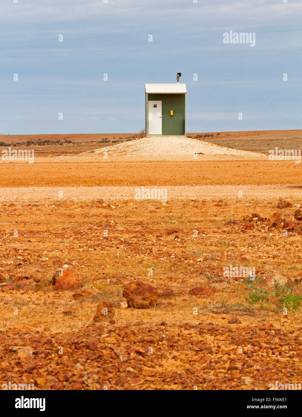Humourous view of isolated public toilet on vast barren red stony outback plains in remote area of Australia under blue sky Stock Photo