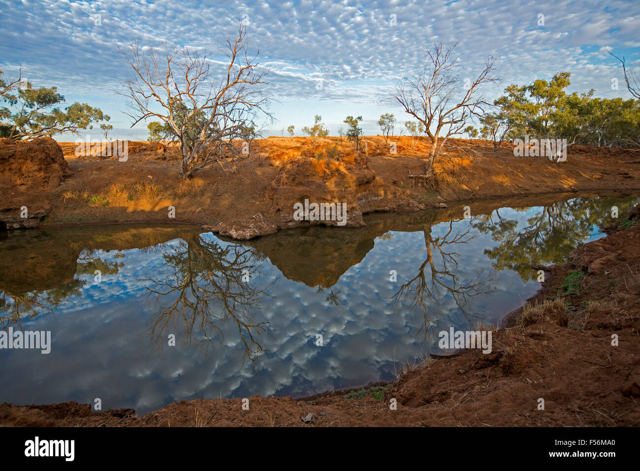 Stunning outback landscape, blue sky freckled with clouds reflected in mirror surface of water hemmed by rugged red boulders Stock Photo