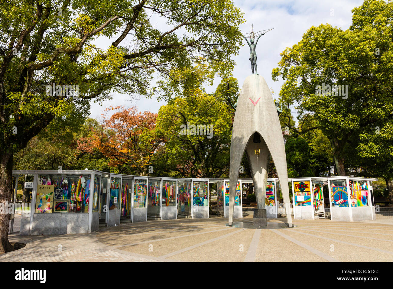 Japan, Hiroshima. A-Bomb, the children's Peace Monument statue and behind it booths contain paper cranes from all over Japan. Sunshine and blue sky. Stock Photo