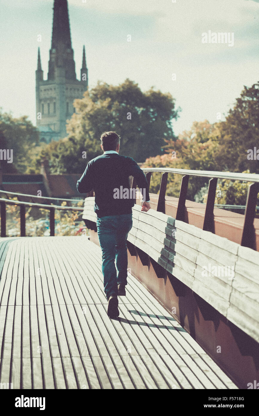 Man running across urban bridge with church in the background Stock Photo