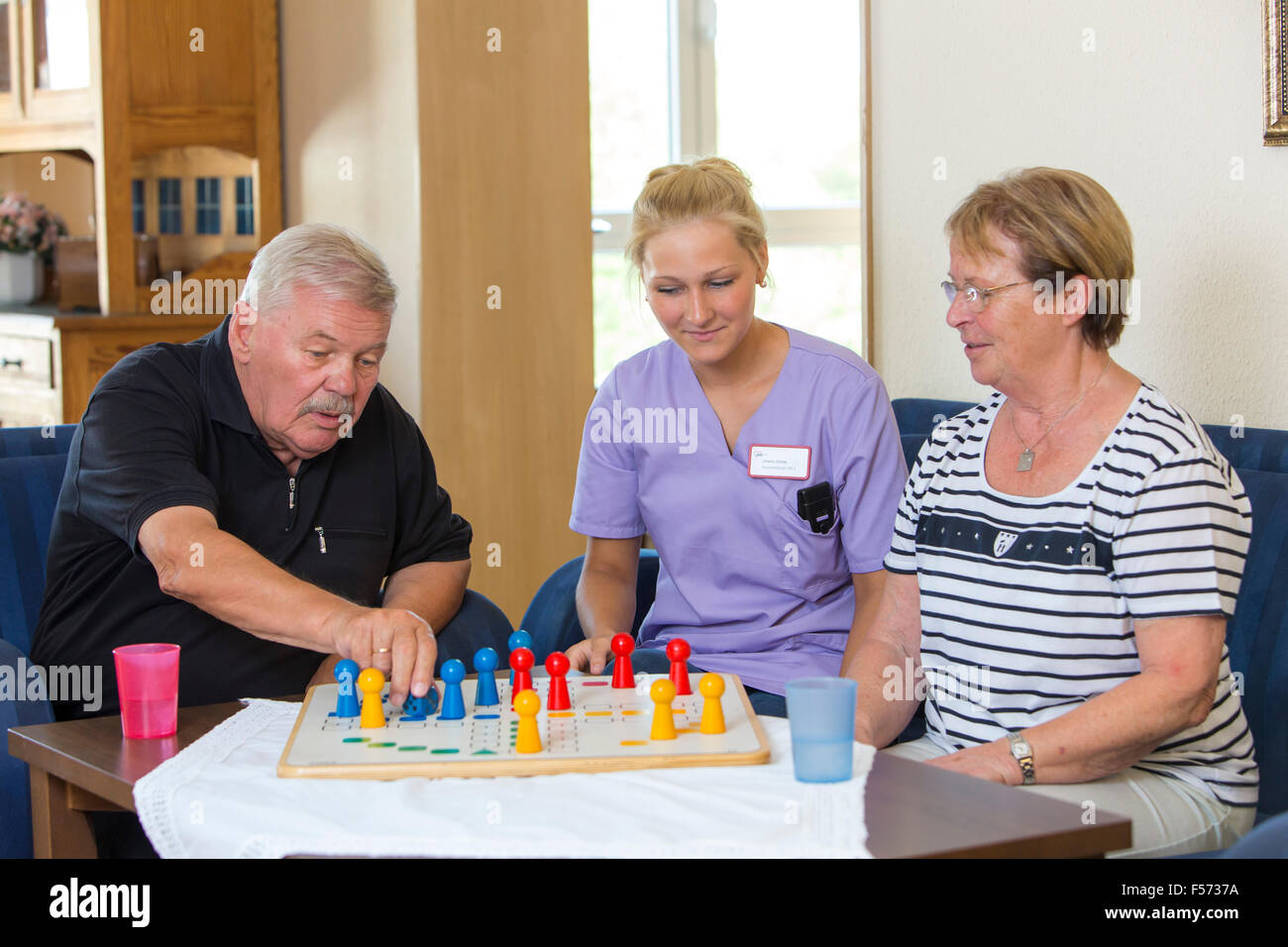 Elderly care in a nursing home, nurse plays with two patients a game