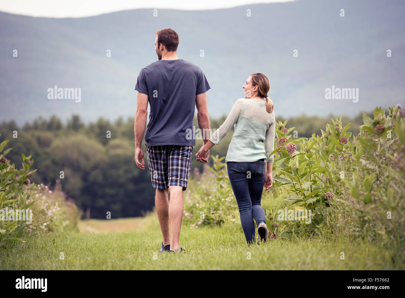 A couple, man and woman walking through a meadow holding hands. Stock Photo