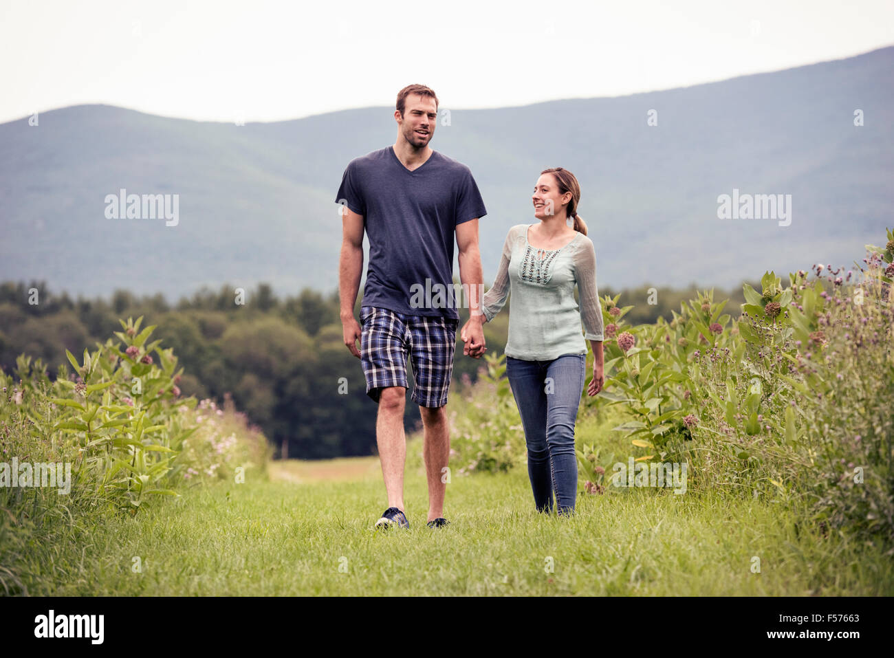 A couple, man and woman walking through a meadow holding hands. Stock Photo
