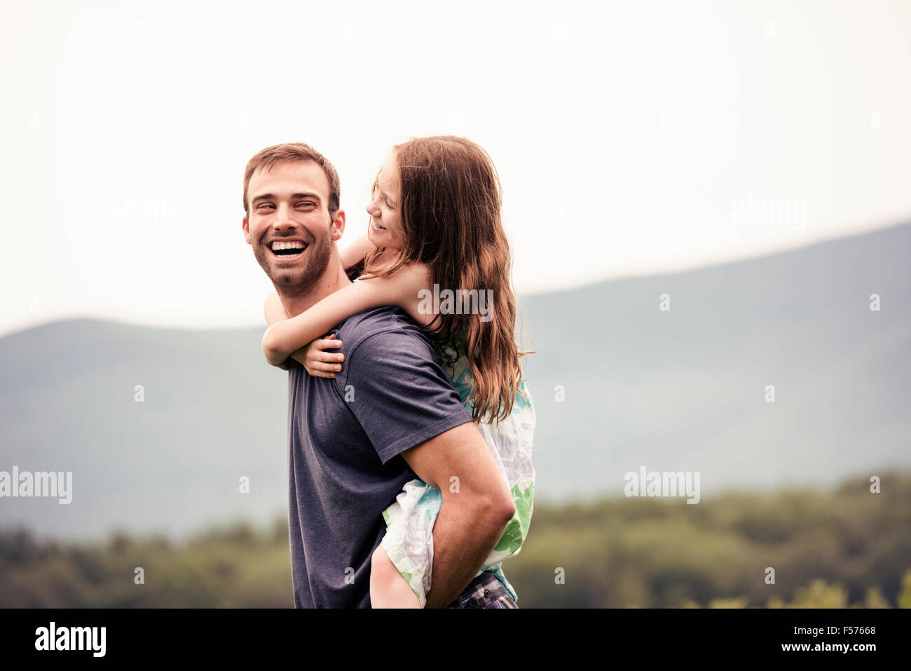 A man giving a young child a piggyback in a meadow. Stock Photo