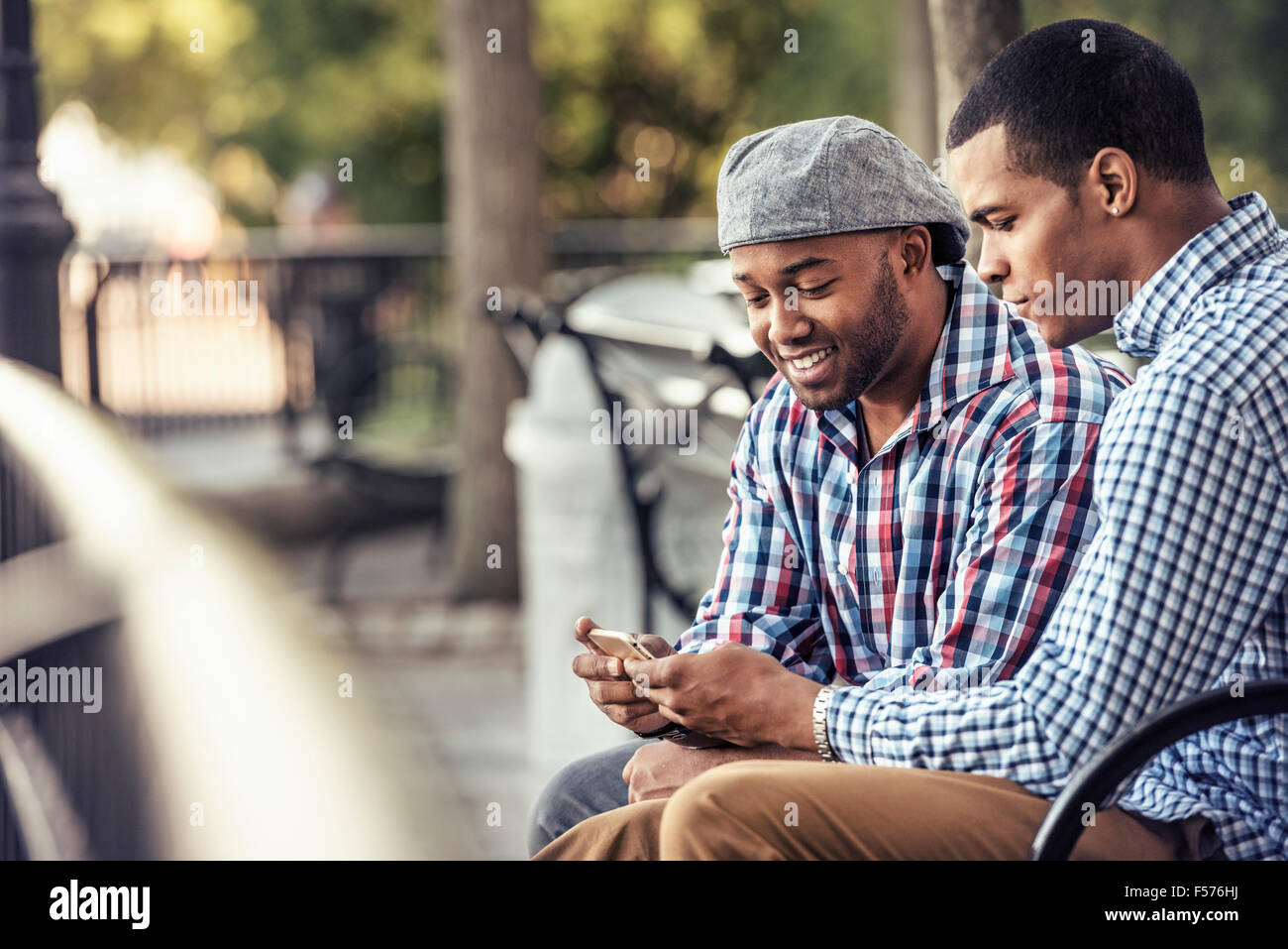 Two men sitting in a park, looking at a smart phone Stock Photo