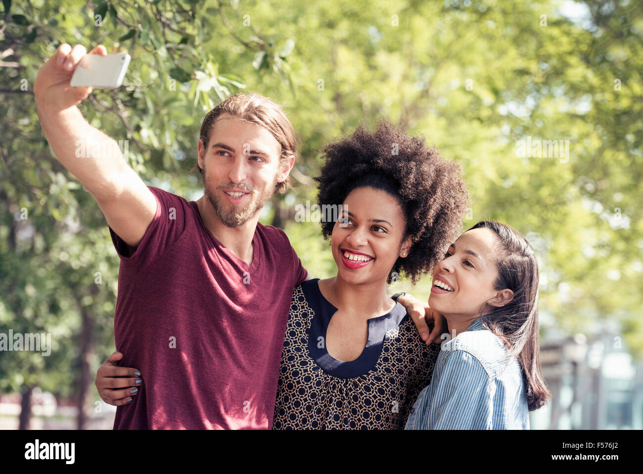 Three people, a man and two women, taking selfies in a city park Stock Photo