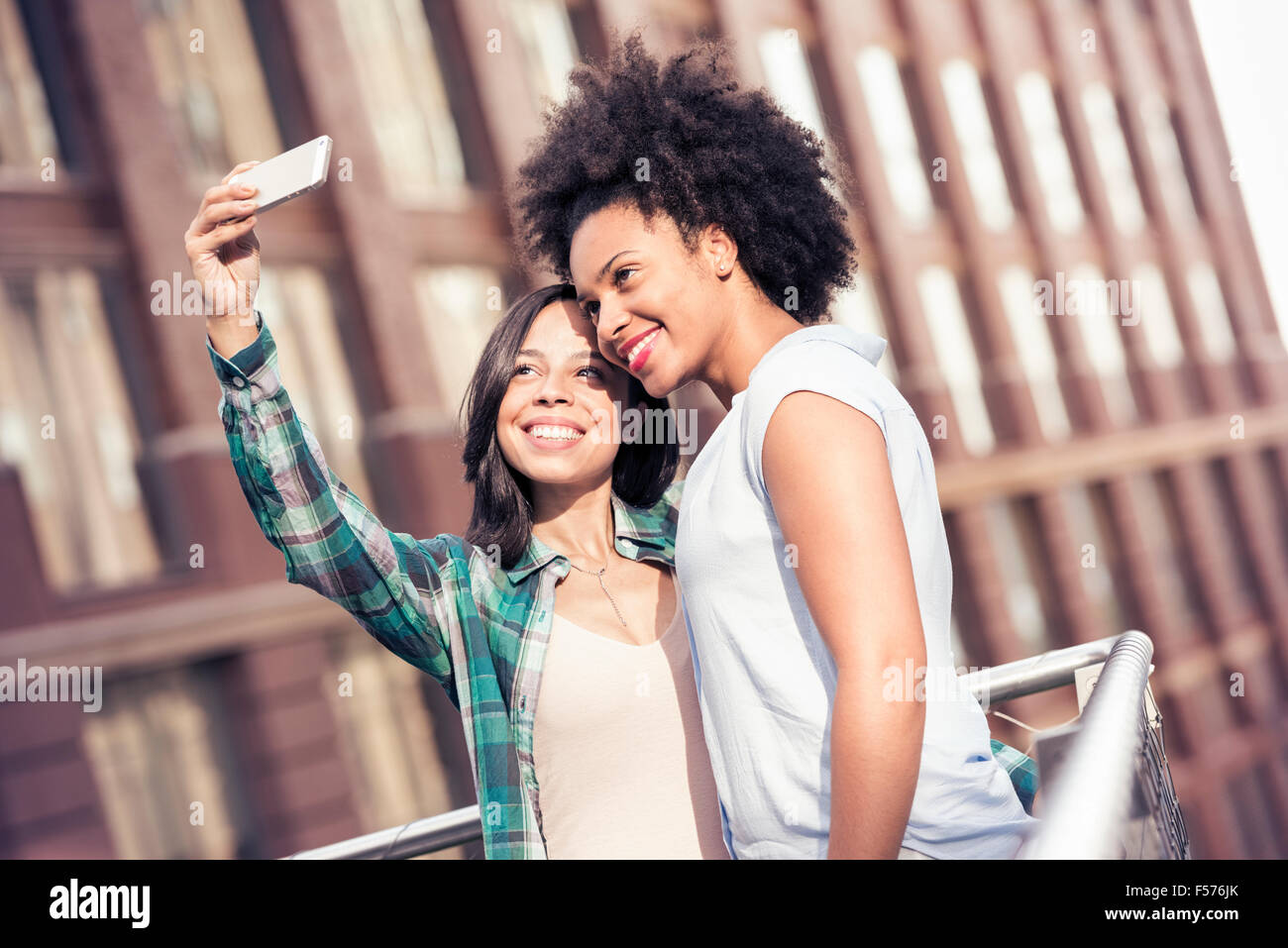 Two women posing and taking a selfie by a large building in the city Stock Photo