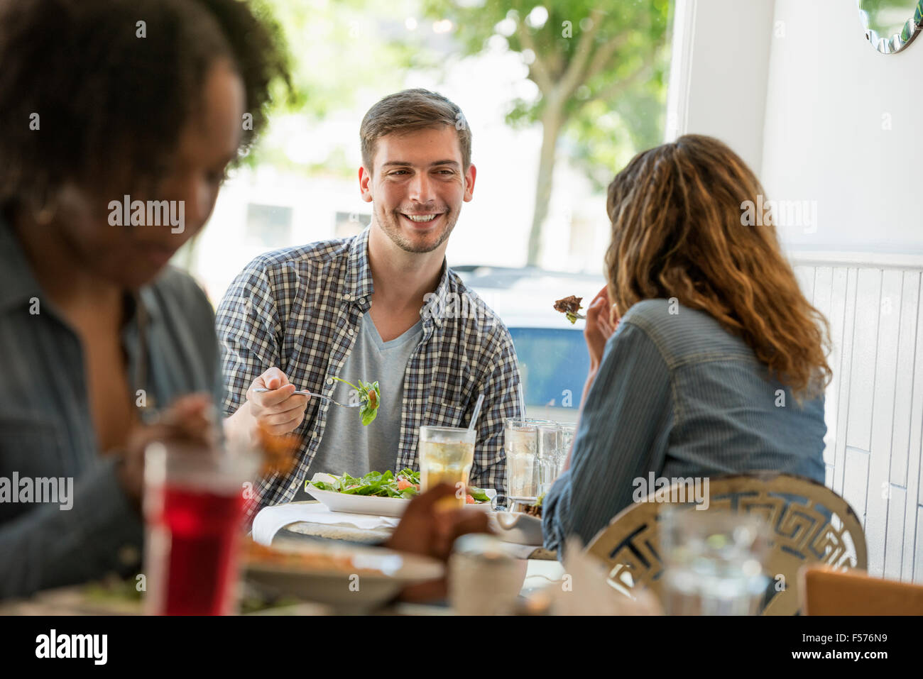 Three people seated at tables at a cafe or diner eating. Stock Photo
