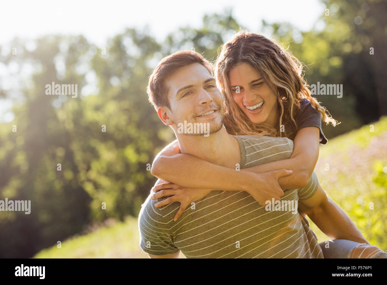 A couple, a man giving a young woman a piggyback, walking through a flower meadow in summer. Stock Photo