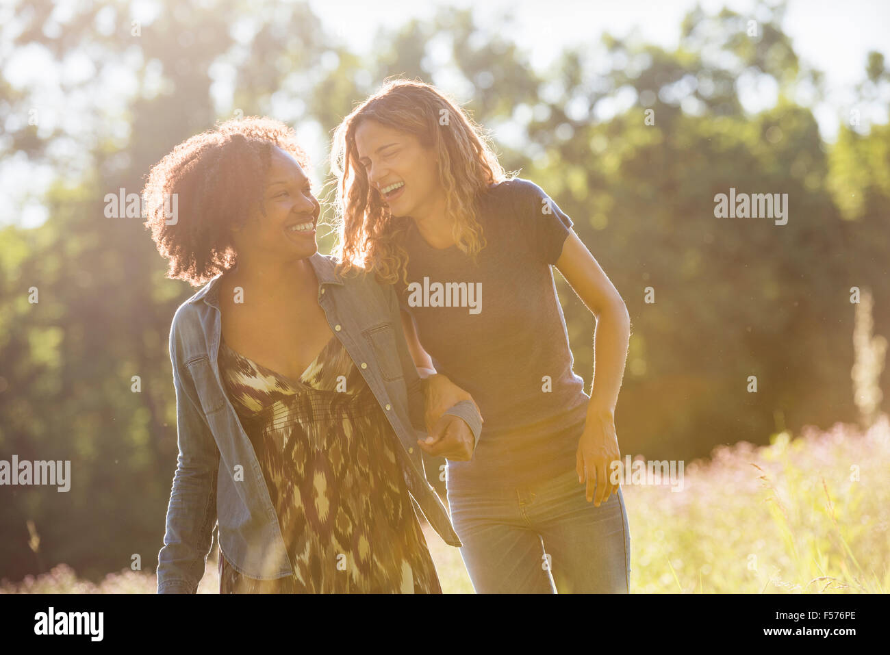 Two women walking through a field talking and laughing. Stock Photo