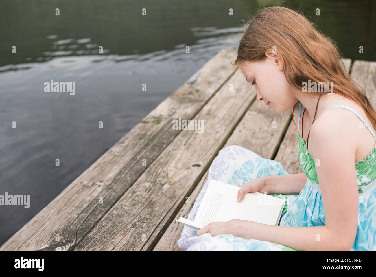 A young girl sitting on the jetty by a lake, reading Stock Photo - Alamy