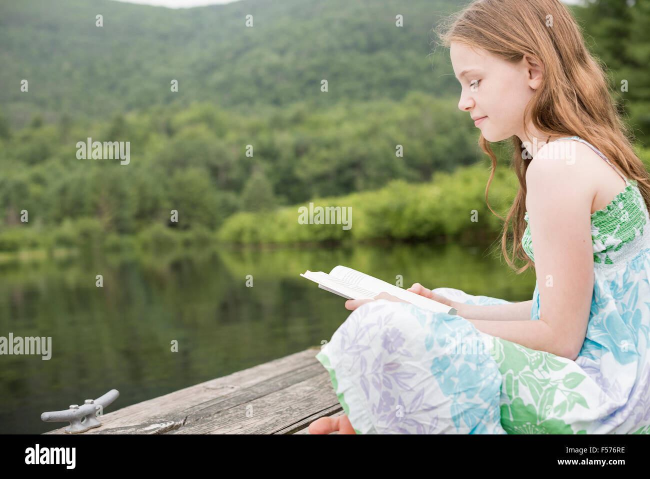 A young girl sitting on the jetty by a lake, reading Stock Photo - Alamy