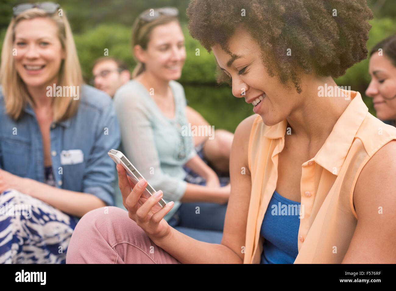 A woman in a group of friends, looking down at her phone, Stock Photo
