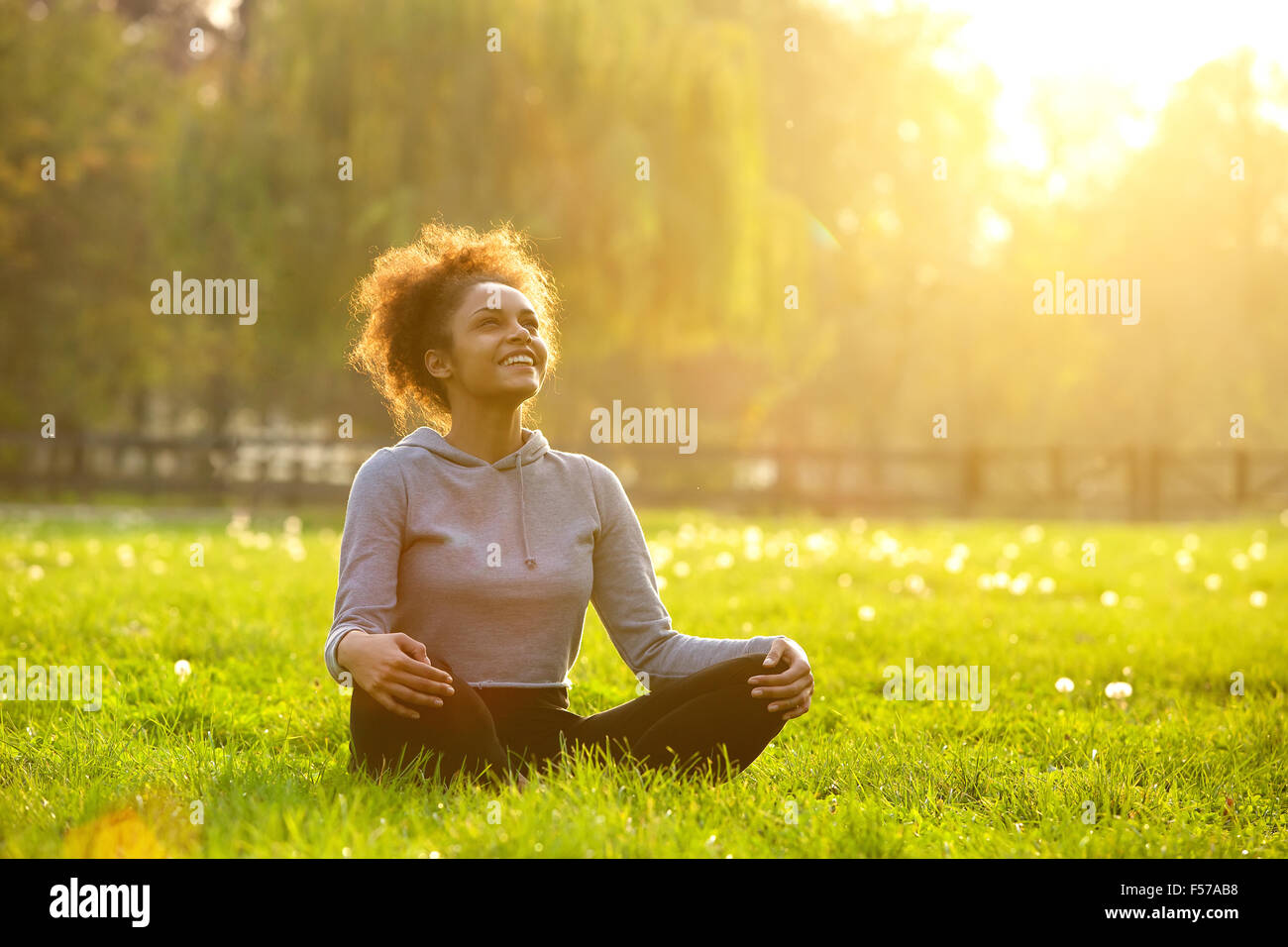 Happy young woman sitting outdoors in yoga position Stock Photo