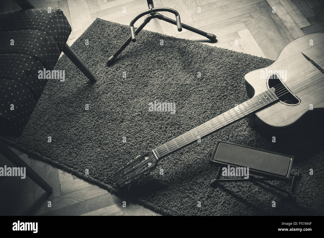 Old acoustic gypsy guitar on carpet in one corner and part of an armchair and guitar stand on the other side. Stock Photo