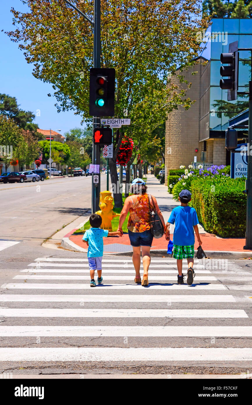 A mother holds the hands of her two children as she crosses a road on the pedestrian walkway in downtown Santa Paula CA Stock Photo