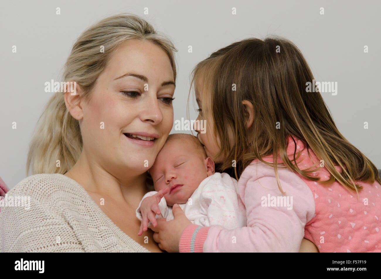Mother and one day old girl back home from hospital birth. Three year old sister kissing her new sister. UK. Stock Photo