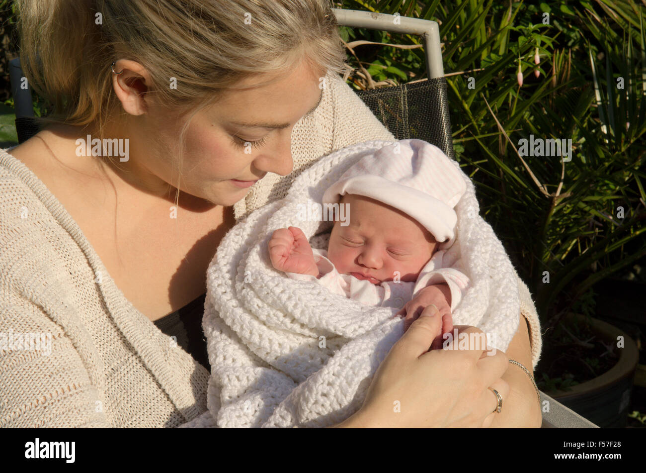 Mother with one day old baby girl sitting in sunshine. Baby slightly jaundiced. UK. Stock Photo