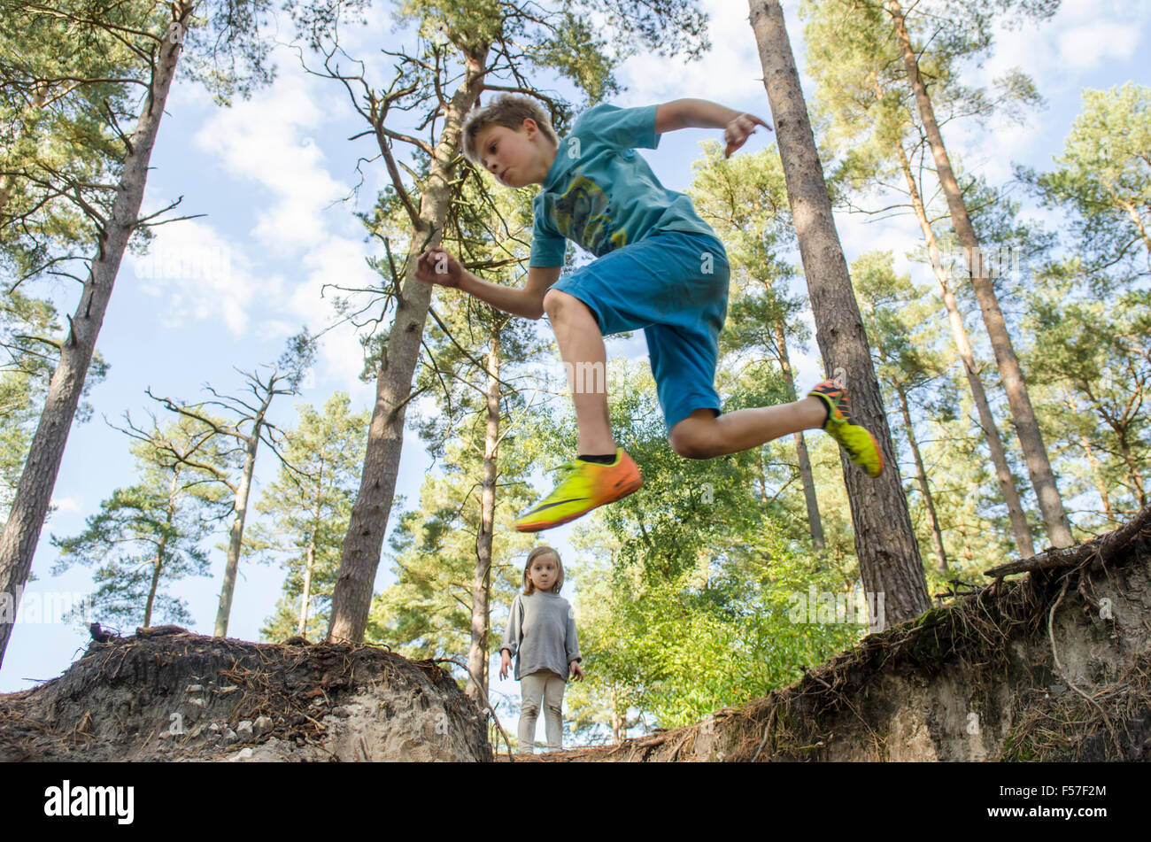nine year old boy jumping off a bank with his three years old sister watching in woodland, Sussex. UK. October. Stock Photo