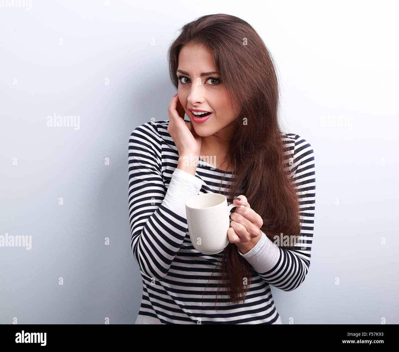 Fun surprising young woman with opened mouth holding cup of tea on blue background Stock Photo
