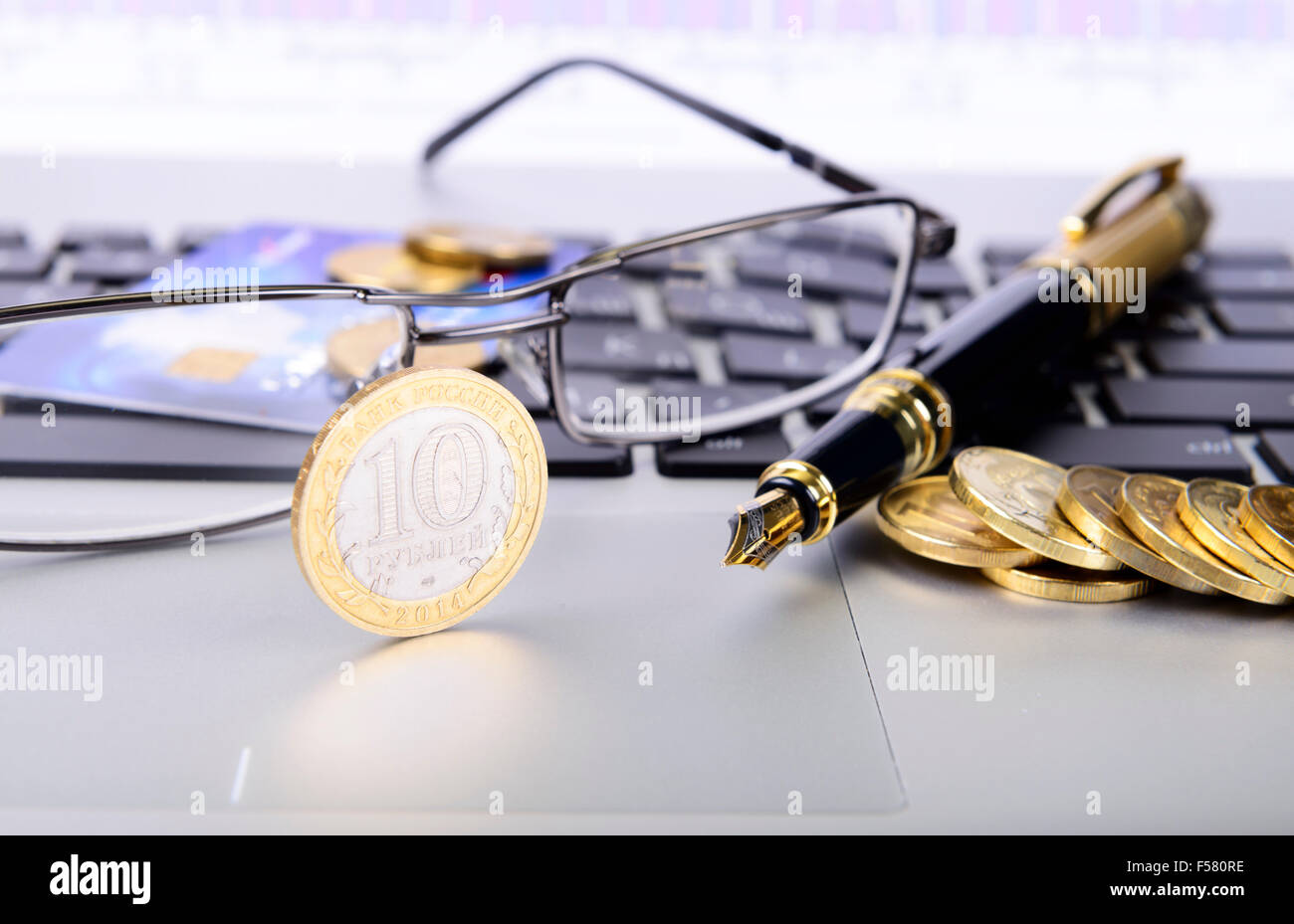 pen, coins, glasses and a bank card on the keyboard Stock Photo