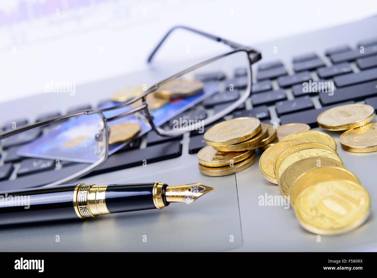 pen, coins, glasses and a bank card on the keyboard Stock Photo