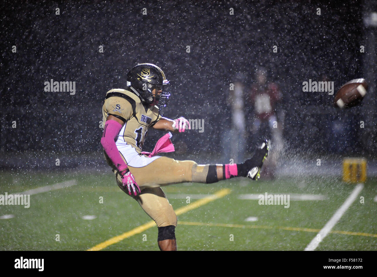 Punter having a significant challenge in kicking  the football due to very wet and windy game conditions. USA. Stock Photo