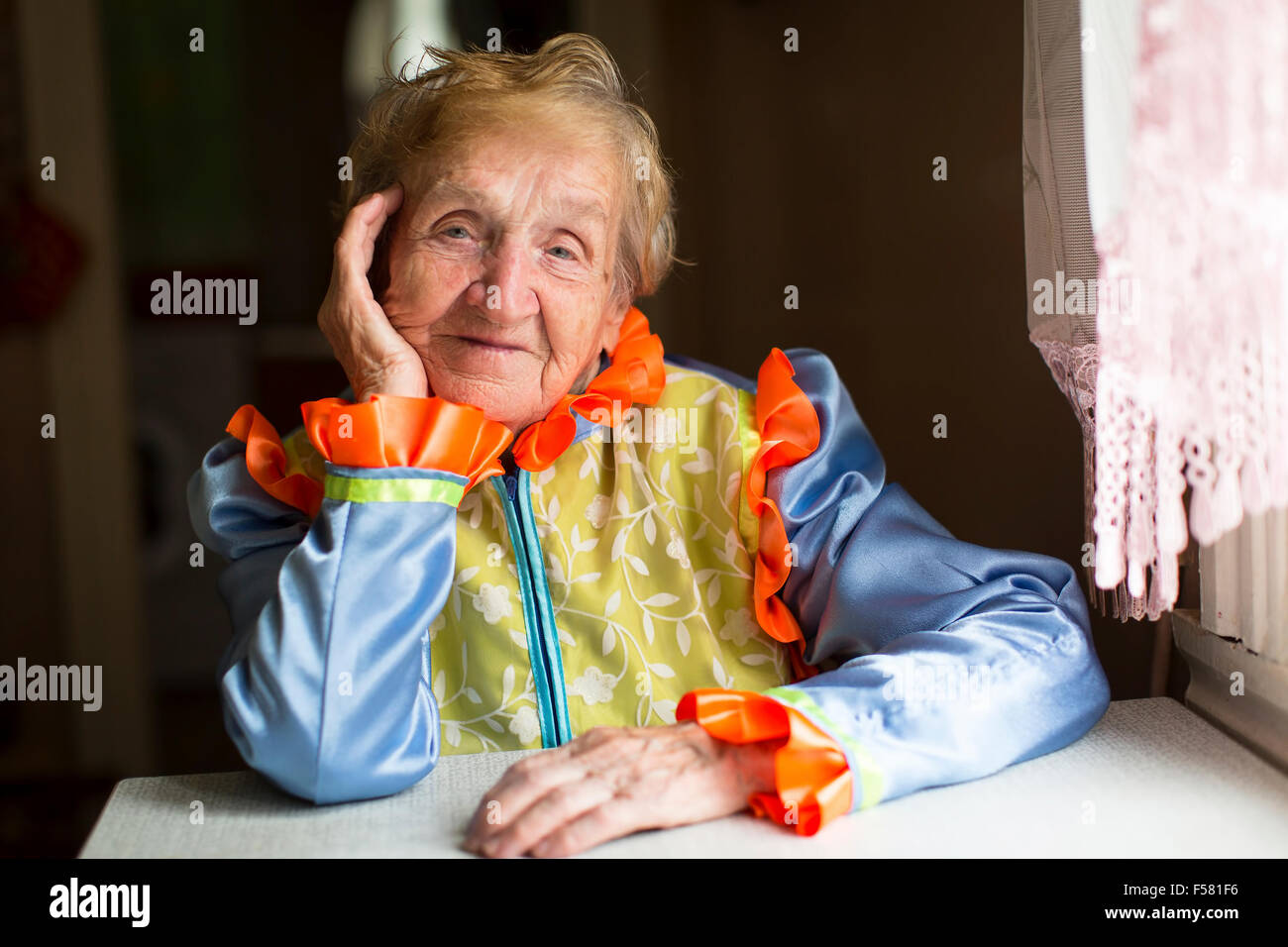 Old woman in ethnic slavic clothes sitting at a table in the house. Stock Photo