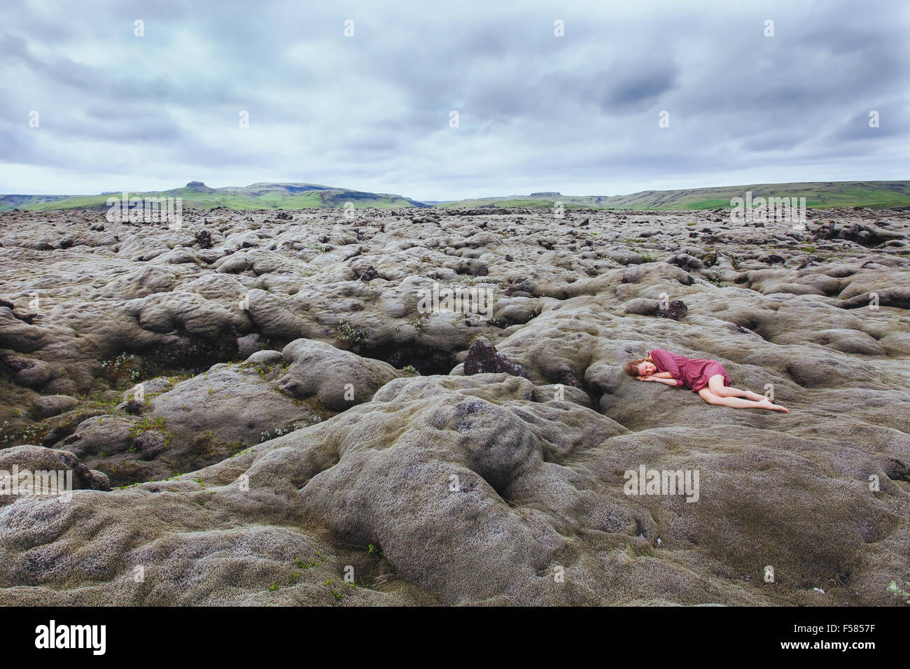 beautiful girl in red dress sleeping in lava field in Iceland, solitude concept Stock Photo